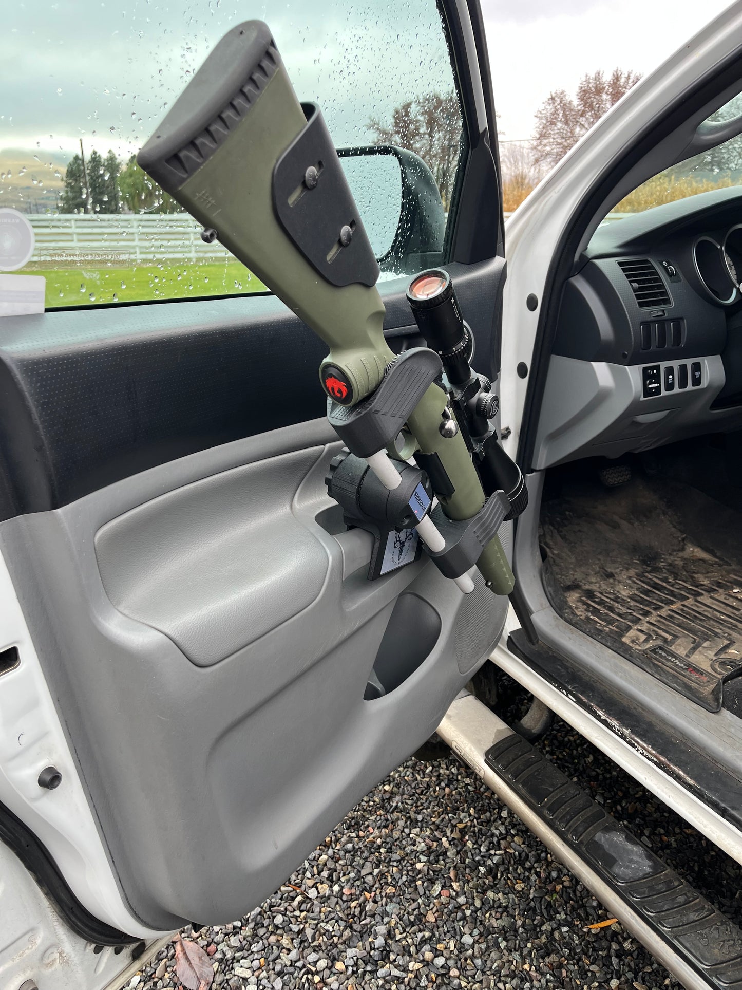 Rifle mounted on truck door with a blurred outdoor background